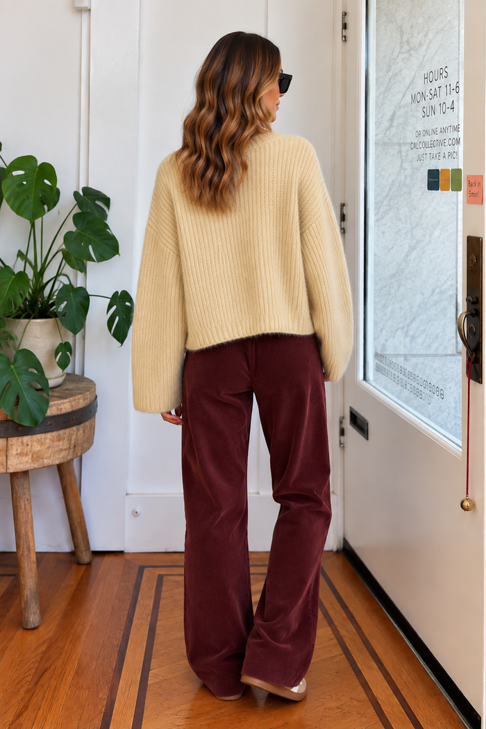 Back view of cream relaxed fit knit sweater styled with burgundy corduroy pants