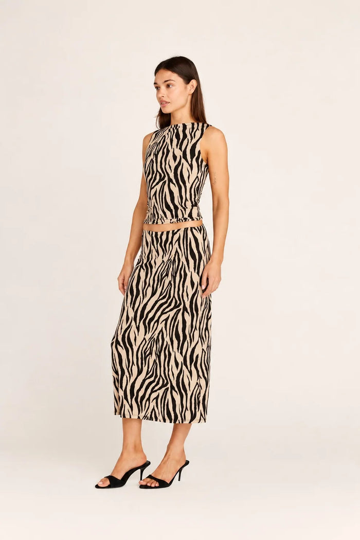 Blonde model wearing the Emma zebra print midi skirt with the matching Carrie Tank in black and cream, styled in a boutique setting.