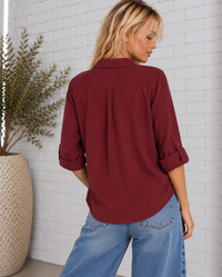 Back view of the Talma Shirt in Bordeaux, featuring a relaxed fit, back yoke, adjustable roll-tab sleeves, and curved shirttail hem.